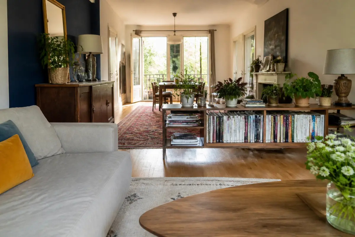 Aménagement d’un salon en longueur avec canapé, bibliothèque, table et nombreuses plantes décoratives